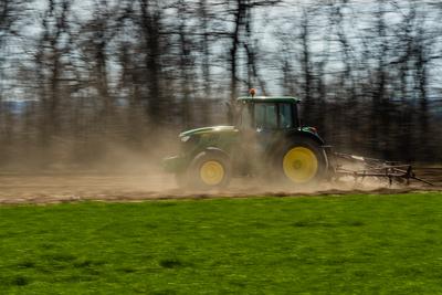 A farmer is plowing with a John Deere tractor. Sunny day on the field. It's a panning shot, that cause the blurry background and foreground.-stock-photo