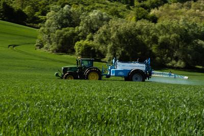 A farmer spraying on the spring wheat field with a John Deere tractor and a mamut topline sprayer. Panning shot.-stock-photo