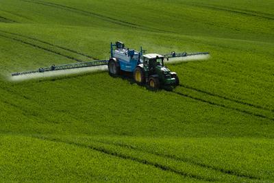 A farmer spraying on the spring wheat field with a John Deere tractor and a mamut topline sprayer.-stock-photo