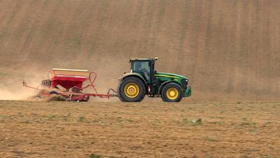 A farmer sowing with a John Deere tractor and a Horsch Pronto 4dc seeding machine. It's a panning shot, that cause the blurry background.-stock-photo