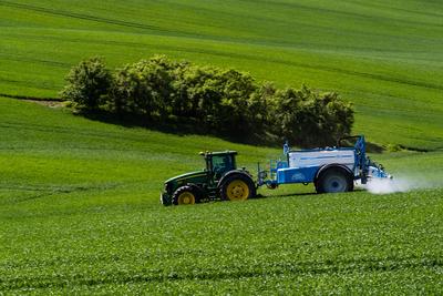 A farmer spraying on the spring wheat field with a John Deere tractor and a mamut topline sprayer.-stock-photo