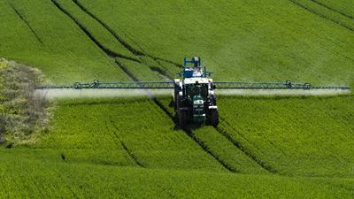 A farmer spraying on the spring wheat field with a John Deere tractor and a mamut topline sprayer.-stock-photo