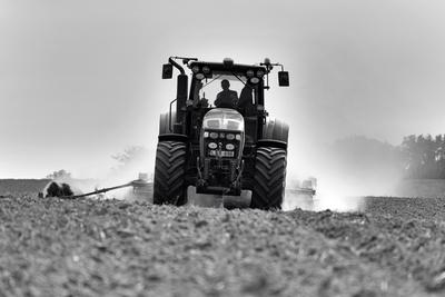 A farmer working on the field with a John Deere tractor. Black and white.-stock-photo