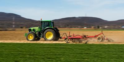 A farmer is plowing with a John Deere tractor. Sunny day on the field. It's a panning shot, that cause the blurry background and foreground.-stock-photo