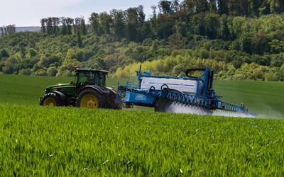 A farmer spraying on the spring wheat field with a John Deere tractor and a mamut topline sprayer.-stock-photo