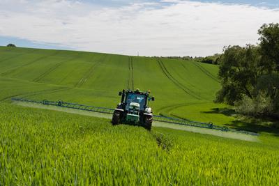 A farmer spraying on the spring wheat field with a John Deere tractor and a mamut topline sprayer.-stock-photo