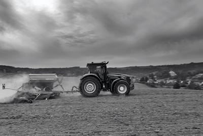 A farmer sowing with a John Deere tractor and a Horsch Pronto 4dc seeding machine. It's a panning shot, that cause the blurry background. Black and white.-stock-photo