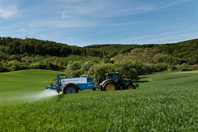 A farmer spraying on the spring wheat field with a John Deere tractor and a mamut topline sprayer. Panning shot.-stock-foto