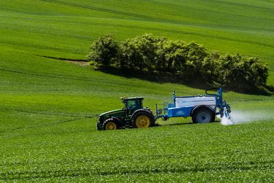 A farmer spraying on the spring wheat field with a John Deere tractor and a mamut topline sprayer.-stock-photo