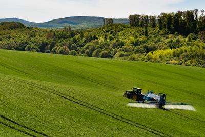 A farmer spraying on the spring wheat field with a John Deere tractor and a mamut topline sprayer.-stock-photo