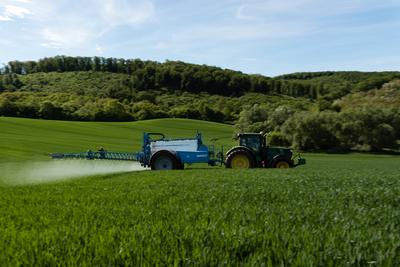 A farmer spraying on the spring wheat field with a John Deere tractor and a mamut topline sprayer. Panning shot.-stock-foto