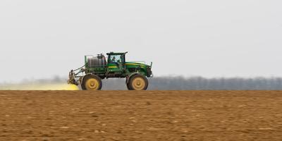 A farmer spraying with a John Deere sprayer. It's a panning shot, that's cause the blurry back and foreground.-stock-photo