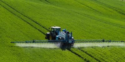 A farmer spraying on the spring wheat field with a John Deere tractor and a mamut topline sprayer.-stock-photo