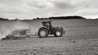 A farmer sowing with a John Deere tractor and a Horsch Pronto 4dc seeding machine. It's a panning shot, that cause the blurry background. Black and white.-stock-foto