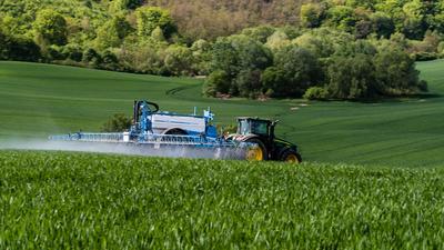 A farmer spraying on the spring wheat field with a John Deere tractor and a mamut topline sprayer.-stock-photo