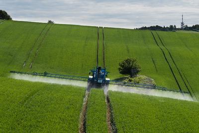 A farmer spraying on the spring wheat field with a John Deere tractor and a mamut topline sprayer.-stock-photo