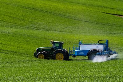 A farmer spraying on the spring wheat field with a John Deere tractor and a mamut topline sprayer.-stock-photo