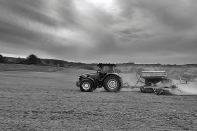 A farmer sowing with a John Deere tractor and a Horsch Pronto 4dc seeding machine. It's a panning shot, that cause the blurry background. Black and white.-stock-photo
