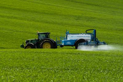 A farmer spraying on the spring wheat field with a John Deere tractor and a mamut topline sprayer. Panning shot.-stock-photo