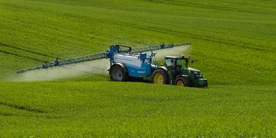 A farmer spraying on the spring wheat field with a John Deere tractor and a mamut topline sprayer.-stock-photo