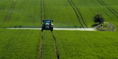 A farmer spraying on the spring wheat field with a John Deere tractor and a mamut topline sprayer.-stock-photo
