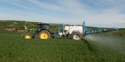 A farmer spraying on the spring wheat field with a John Deere tractor and a mamut topline sprayer. Panning shot.-stock-foto