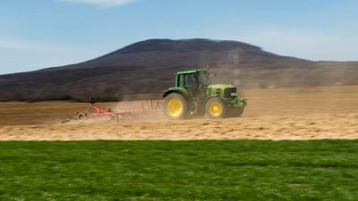 A farmer is plowing with a John Deere tractor. Sunny day on the field. It's a panning shot, that cause the blurry background and foreground.-stock-photo