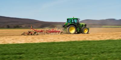 A farmer is plowing with a John Deere tractor. Sunny day on the field. It's a panning shot, that cause the blurry background and foreground.-stock-photo