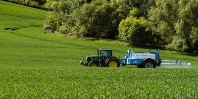 A farmer spraying on the spring wheat field with a John Deere tractor and a mamut topline sprayer. Panning shot.-stock-foto