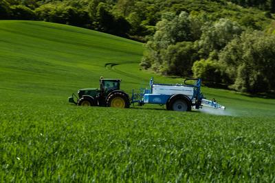A farmer spraying on the spring wheat field with a John Deere tractor and a mamut topline sprayer. Panning shot.-stock-foto