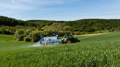 A farmer spraying on the spring wheat field with a John Deere tractor and a mamut topline sprayer. Panning shot.-stock-foto