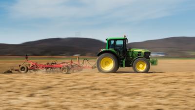 A farmer plowing with a John Deere tractor. Sunny day on the field.-stock-photo