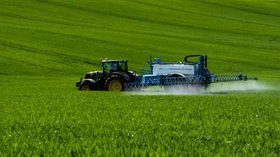 A farmer spraying on the spring wheat field with a John Deere tractor and a mamut topline sprayer. Panning shot.-stock-foto