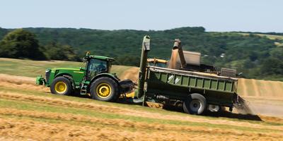 Farmers harvesting and unloading the threshed seeds with a New Holland combine, a John Deere tractor and a Fliegl ULW trailer simultaneous.-stock-photo