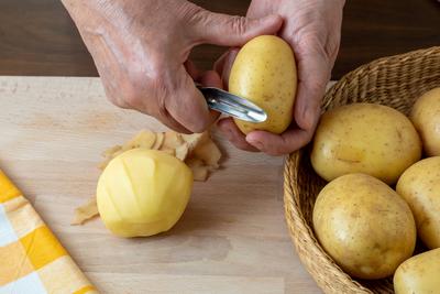 Hands peel potato, peelings on wooden cutting board. Hands peel potato, peelings on wooden cutting board. Copyright: xZo-stock-photo