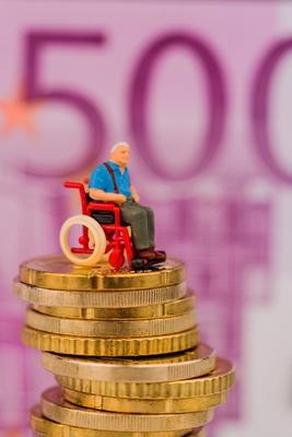 Frau im Rollstuhl auf Geldstapel Symbolfoto f?r Behinderung Pflegegeld und Kosten im Gesunheitswes-stock-foto