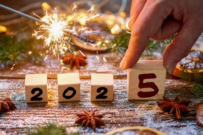 9 December 2024: Wooden cube with the year 2025, accompanied by sparks from a sparkler and a hand placing the last cube.-stock-foto