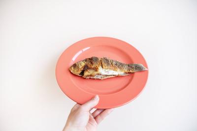 A whole fried carp with a fried crust, served on a bright red plate. A hand holds a plate on a white background. A whole-stock-foto