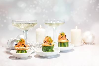 Festive canapes from smoked salmon, cucumber, crackers and caviar, in the background gasses with champagne, candles and-stock-foto