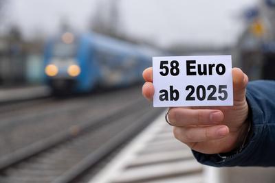Bavaria, Germany - December 17, 2024: A person holds a sign with the text 58 EURO AB 2025 in front of a train station an-stock-foto