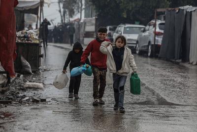 Palestinians, including children, line up to collect drinking water under rain showers inside a camp for displaced people west of Deir al-Balah-stock-foto