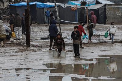 Palestinians, including children, line up to collect drinking water under rain showers inside a camp for displaced people west of Deir al-Balah-stock-foto