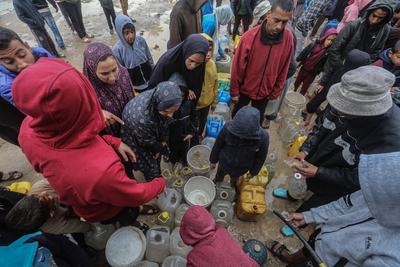 Palestinians, including children, line up to collect drinking water under rain showers inside a camp for displaced people west of Deir al-Balah-stock-foto
