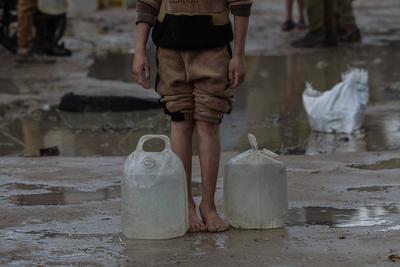 Palestinians, including children, line up to collect drinking water under rain showers inside a camp for displaced people west of Deir al-Balah-stock-foto