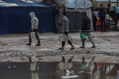 Palestinians, including children, line up to collect drinking water under rain showers inside a camp for displaced people west of Deir al-Balah-stock-foto
