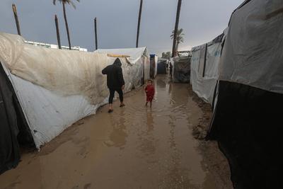 Internally displaced Palestinians walk outside their tents on a windy day west of Deir al-Balah, central Gaza Strip-stock-foto