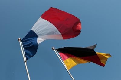 Flaggen Deutschland s und Frankreich s wehen eintraechtig vor blauem Himmel und Sonnenschein im Wind-stock-foto