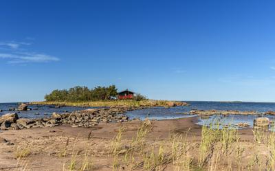 picturesque coastal landscape on the Baltic Sea with a small red cottage on an island behind a sandy beach under a blue-stock-photo