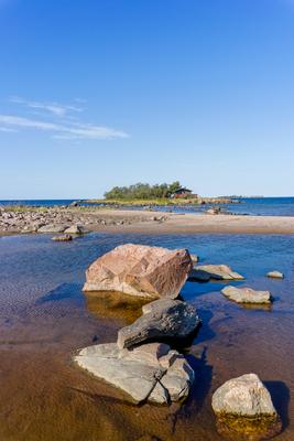 picturesque coastal landscape on the Baltic Sea with a small red cottage on an island behind a sandy beach under a blue-stock-photo