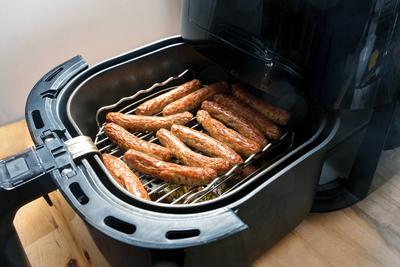Kleine W?rstchen aus Schweinefleisch, in Deutschland N?rnberger Rostbratwurst genannt, in einer Hei?luftfritteuse auf einem Rost gebraten, schnelle Methode zum Braten von Lebensmitteln mit weniger ?l, aber mit faltiger Haut, ausgew?hlter Schwerpunkt-stock-foto
